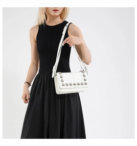 Detail of white leather shoulder bag with silver rivet studs on black dress background