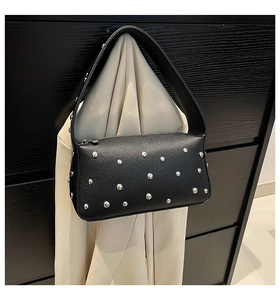 Detail of black pebbled leather handbag with silver studs hanging on a wooden cabinet