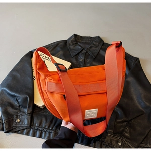 Détail du sac bandoulière orange en forme de croissant avec logo et large sangle