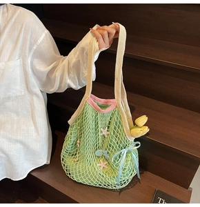 Close-up of green crochet tote bag featuring pink starfish charms and silk bow detail