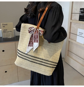 Detail of straw tote bag featuring black stripes and brown leather shoulder strap