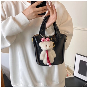 Detail van een zwarte glanzende emmertas met een schattige witte teddybeer hanger