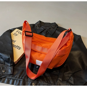 Vue détaillée du sac bandoulière en nylon orange vif sur une veste en cuir noir
