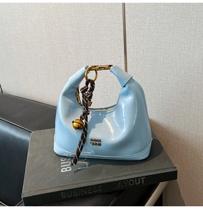 Dettaglio della borsa in vernice azzurra con logo dorato e ciondolo a campanellino