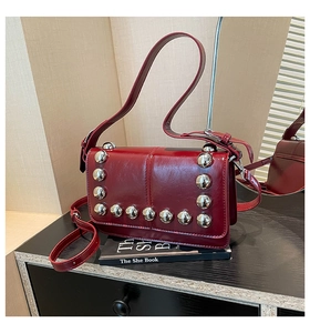 Detail of dark red biker shoulder bag featuring large silver spherical metal studs