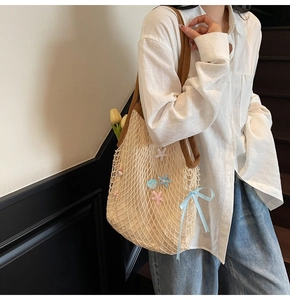 Detail of cream woven tote bag with brown straps, star charms, and blue ribbon decoration
