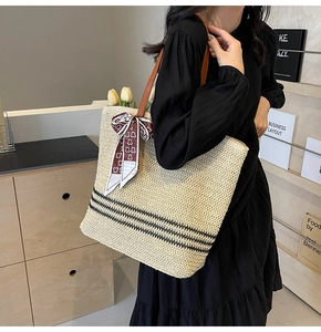Detail of a beige woven tote bag with leather handles and a red silk heart-print scarf