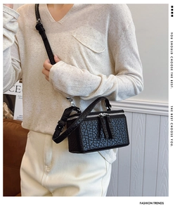 Detailed close-up of a black textured vanity case bag with dual zipper and adjustable strap