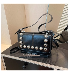 Close-up of black glossy leather crossbody bag with oversized silver studs and flap closure