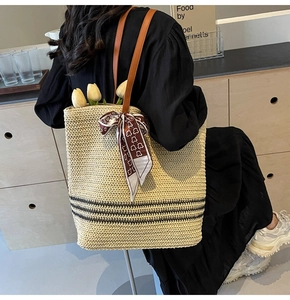 Detail of a beige straw tote bag with black stripes and silk scarf on a shoulder