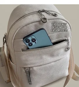 Detail of front zipper pocket on beige leather backpack holding a large smartphone