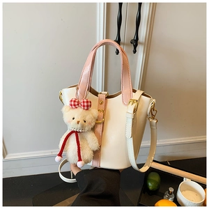 Detail van zachte crèmekleurige bucket bag van kunstleer met roze handgrepen en beer