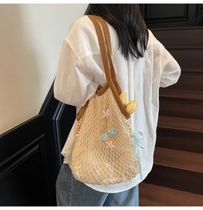Detail of woven mesh tote with star charms and brown straps held by a model