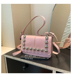Close-up of pink leather crossbody bag featuring large silver metal studs and strap