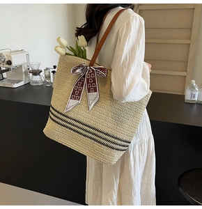 Detail of a large straw tote bag with brown leather straps and red ribbon on model