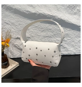 Detail shot of white pebbled leather handbag with silver rivets and vintage top handle