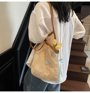 Close-up of beige woven tote bag with blue ribbon bow and colorful pendant detail