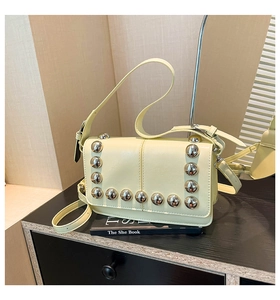 Detail of pale yellow crossbody bag with silver punk studs on a textured leather surface
