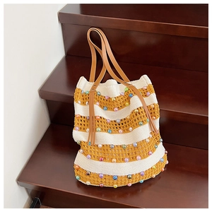 Détail du sac cabas en tricot rayé avec perles colorées et anse en cuir sur escalier