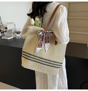 Detail of straw tote bag with brown leather straps, horizontal stripes and a decorative scarf