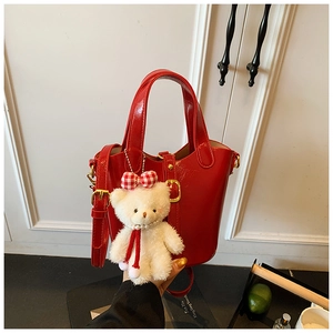 Detail van rode glanzende emmertas met gouden gespen en een schattige teddybeerhanger