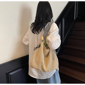 Dettaglio della grande borsa in paglia con tracolla a righe e sciarpa in seta decorativa