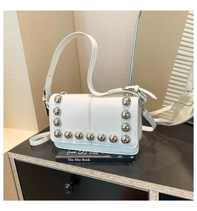 Close-up of white leather crossbody bag with silver rivet studs on dark wood surface