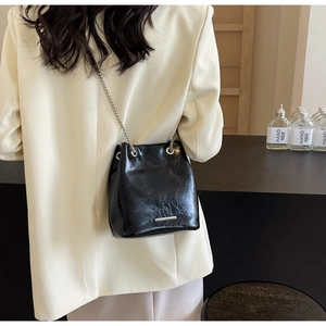 Macro detail of black leather bucket bag showing drawstring closure and silver chain strap
