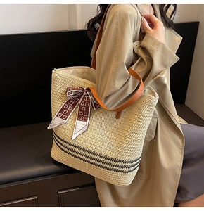 Detail of straw tote bag featuring black stripes, leather straps, and decorative silk scarf
