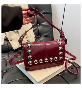 Detail of burgundy glossy leather square bag with silver studs on a white book base