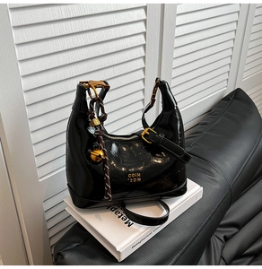 Dettaglio borsa hobo in pelle lucida nera con finiture dorate e ciondolo a campana