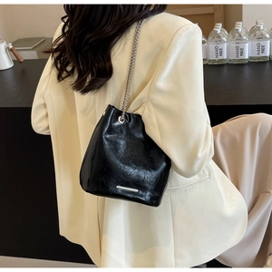 Modern black leather bucket bag with silver chain strap shown worn as a shoulder bag