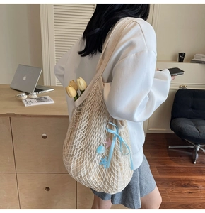 Detail of cream woven tote bag with blue ribbon bow and seashell charms in warm room