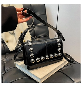 Detail of black glossy handbag with silver metallic spherical studs on a white book