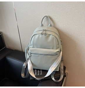 Detail view of a pale green faux leather backpack with textured straps and zippers
