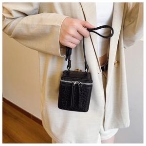 Detail of a black cube box bag with crocodile embossed texture and silver dual zippers