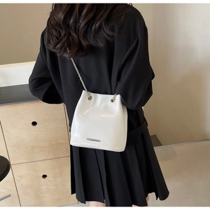 Close-up of a white glossy bucket bag with silver chain strap worn by a model