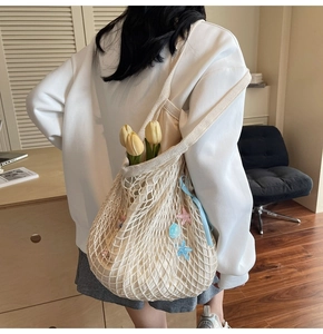 Detail of beige woven mesh tote bag with ocean charms on a casual outfit background
