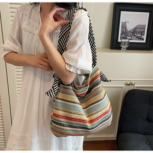 Close-up of a colorful striped straw tote bag with a black and white woven shoulder strap