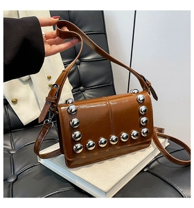 Detail of brown glossy crossbody bag featuring silver metal ball rivets on flap edge