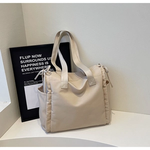Dettaglio borsa shopper beige con tasche laterali a coulisse e cerniera su supporto espositivo