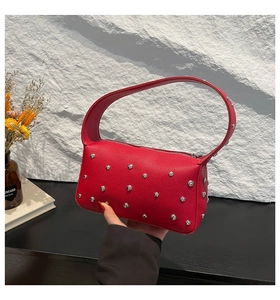 Detail of red lychee leather handbag with silver metal rivets and zipper closure