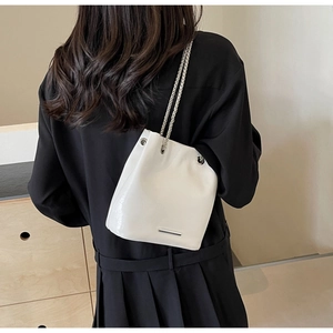 Detail of white glossy leather bucket bag with silver chain strap on a model shoulder