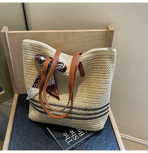 Detail of beige straw tote with black stripes, leather handles, and silk scarf accent