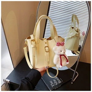 Detail van crèmekleurige bucket bag met decoratieve gesp en pluchen beer op hout