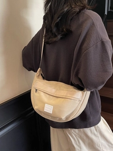Sac à bandoulière beige en demi-lune avec sangle réglable et logo sur un mannequin femme