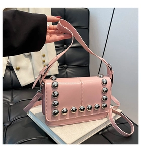 Detail of pink crossbody bag with silver rivet studs on a white blazer and book background