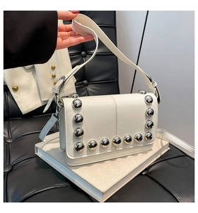 Detailed shot of white rectangular flap bag with large silver stud embellishments