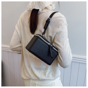 Detail of a black woven textured mini box crossbody bag with silver zipper on a model