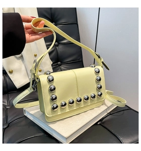 Detailed view of pale yellow leather bag featuring silver spherical rivets on book tray